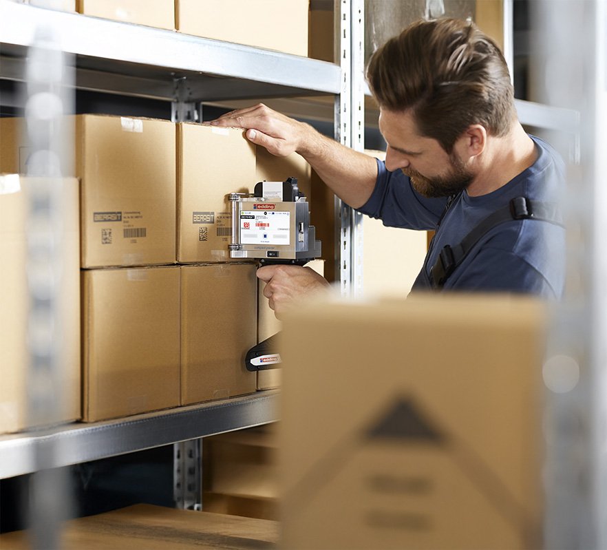 Impresora manual Edding Portable 50 realizando impresión de múltiples líneas de texto en cajas de cartón.